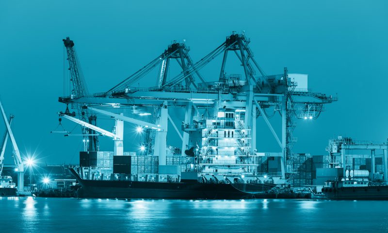 Cargo ship and crane at port reflect on river, twilight time.